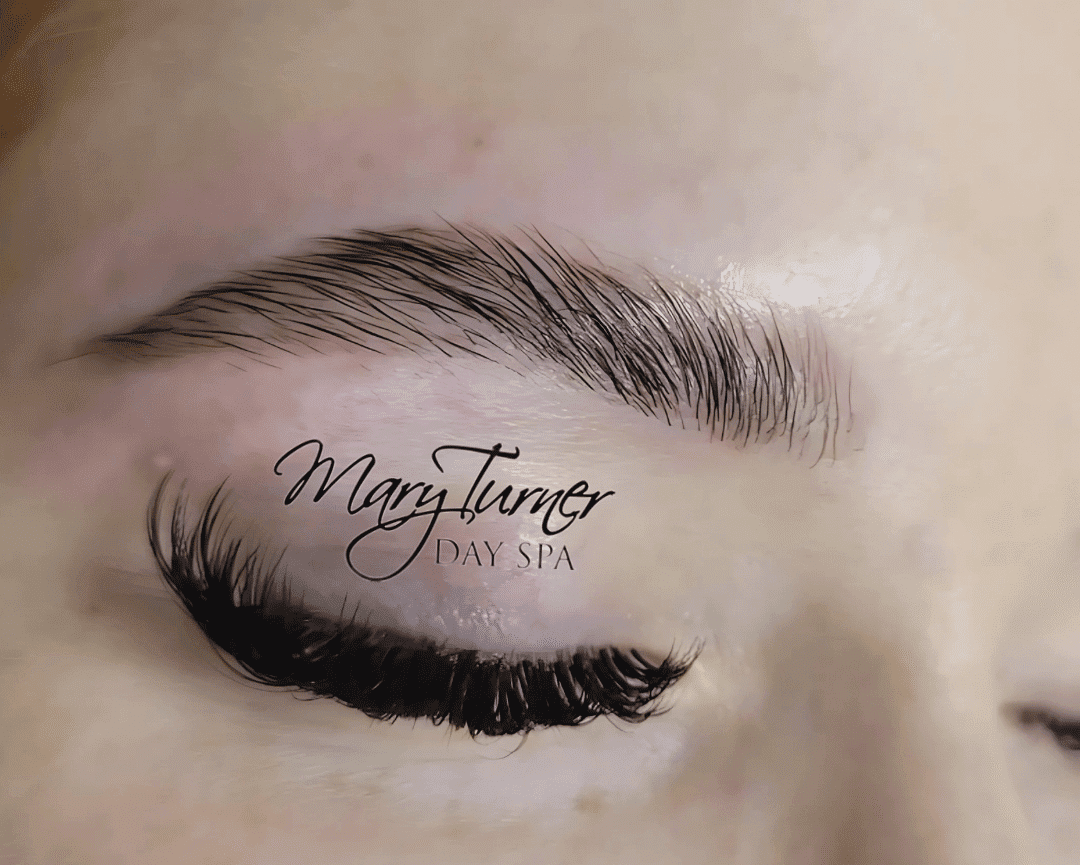 Close-up of a person’s eye with lash extensions and groomed eyebrow, logo reads "Mary Turner Day Spa".